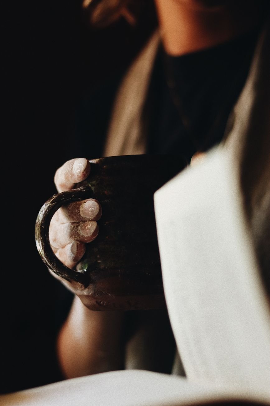 Hands holding a coffee mug near an open book — a warm morning ambiance